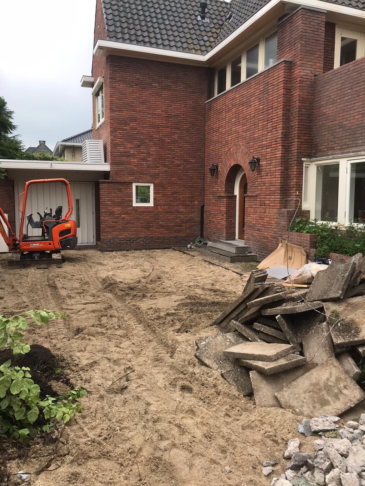 Bouwplaats naast een bakstenen woning met een minigraver