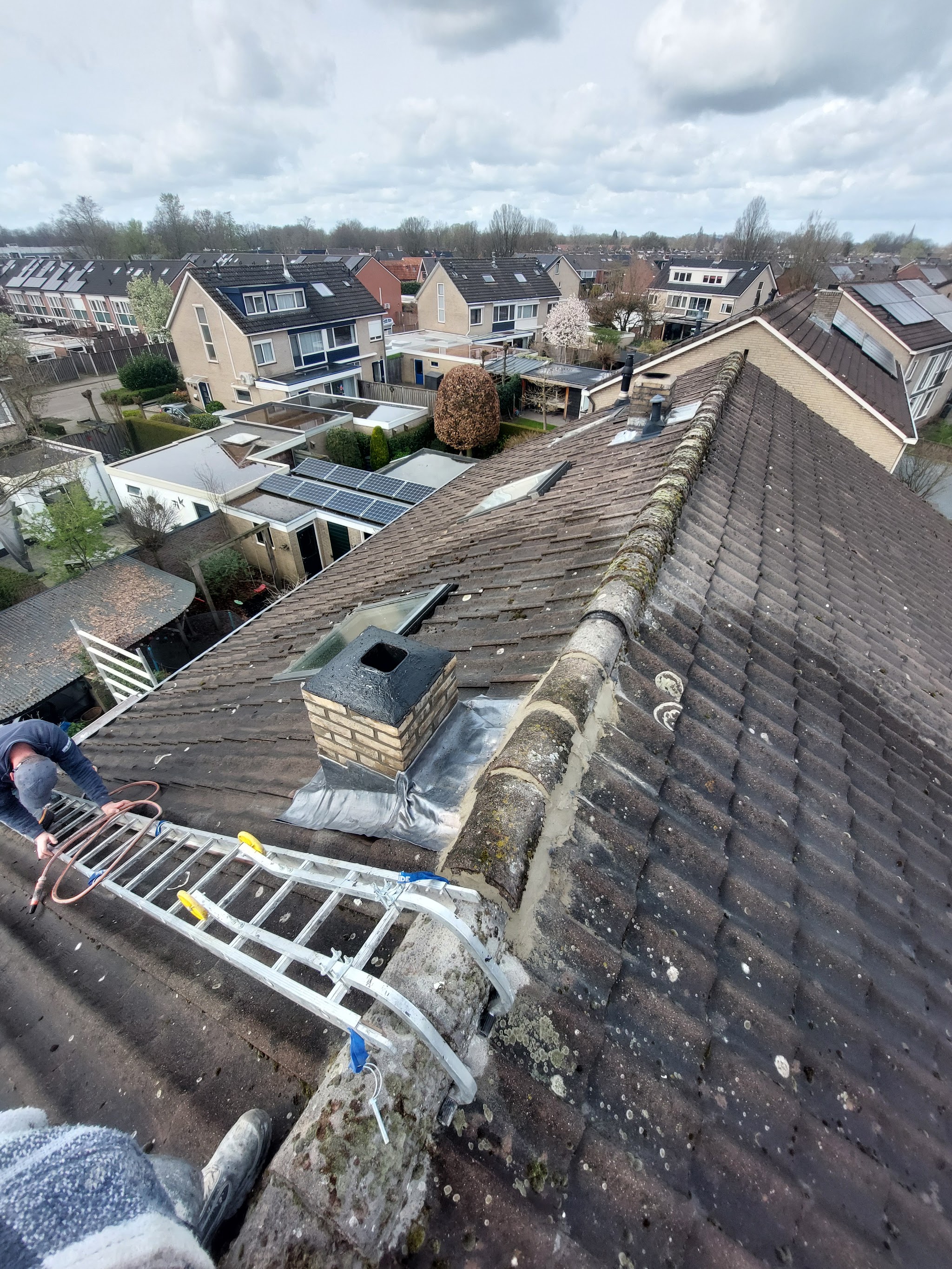 Uitzicht vanaf een pannendak met ladder tijdens werk aan een schoorsteen