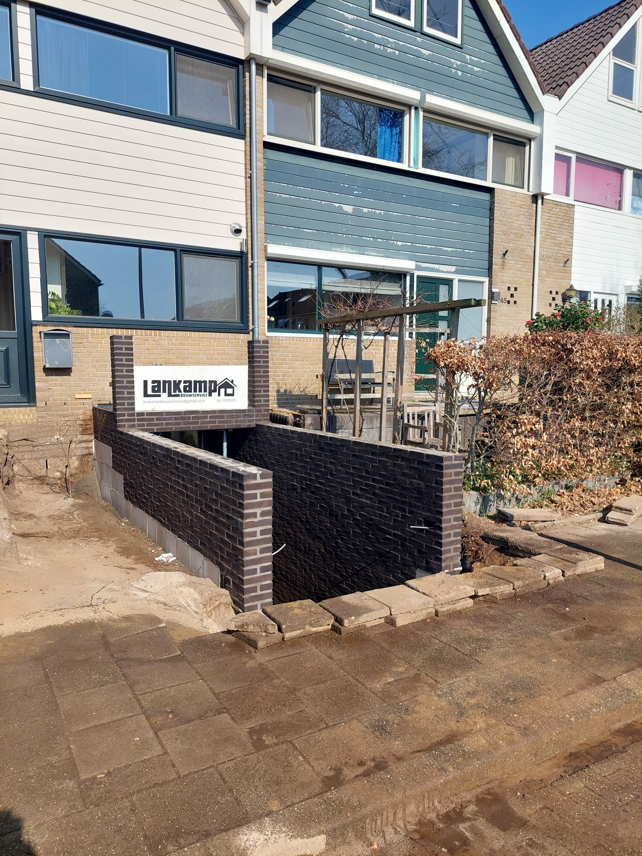 Gemetselde keermuur in donkere steen met bord van Lankamp Bouwservice